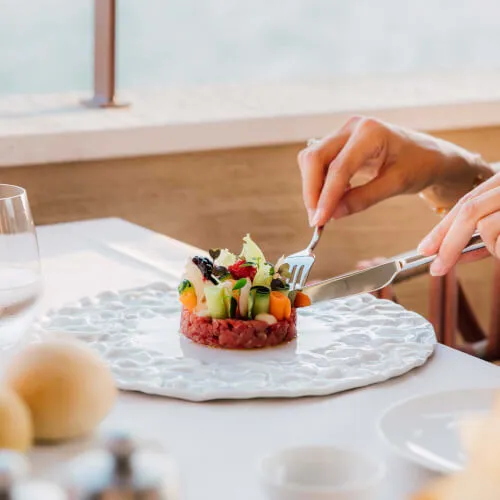 Person cutting a meal at 7Pines Resort Sardinia, showcasing Mediterranean dining.