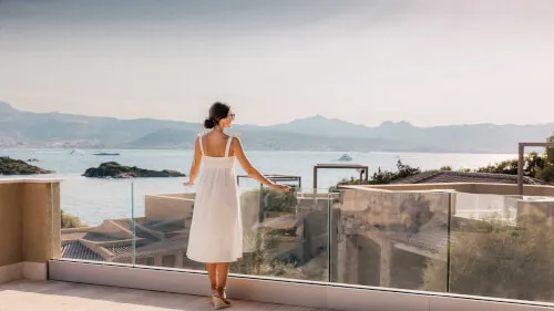 Woman in white dress at 7Pines Resort Sardinia, overlooking the crystal-clear waters of Baja Sardinia.