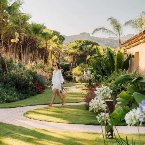 Woman walking path in lush garden at 7Pines Resort Sardinia, capturing the essence of the island's nature.