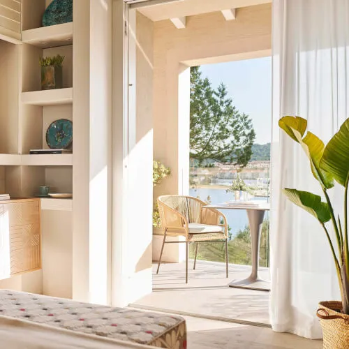A room at 7Pines Resort Sardinia featuring a bed, table, chairs, and a view showcasing the Mediterranean lifestyle.