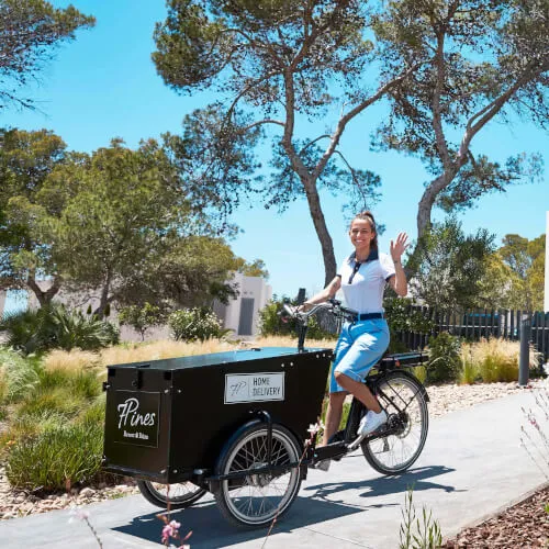 Woman cycling with a trailer offering a glimpse into 7Pines Resort Sardinia's home delivery service.