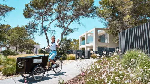 Woman on bike waving, home delivery by 7Pines Resort Sardinia.