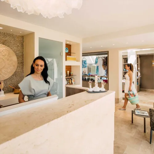 Woman standing behind a counter at 7Pines Resort Sardinia, offering spa and wellness facilities.