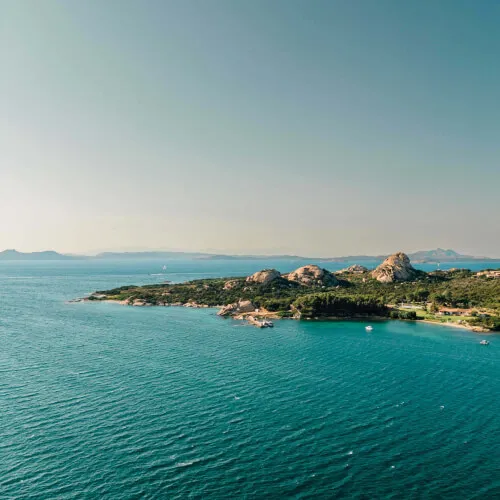 A serene island surrounded by water near 7Pines Resort Sardinia, showcasing nature's beauty.