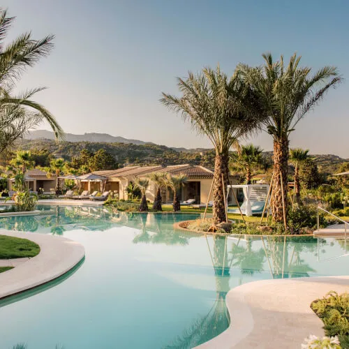 The exclusive Laguna Pool at 7Pines Resort Sardinia, surrounded by palm trees and lush gardens, offers a serene adults-only retreat.