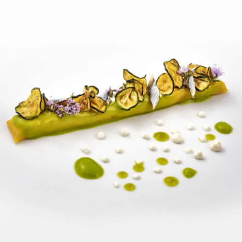 Piatto gourmet verde con fiori e salsa al 7Pines Resort Sardegna, sottolinea la raffinata cucina italiana e mediterranea.