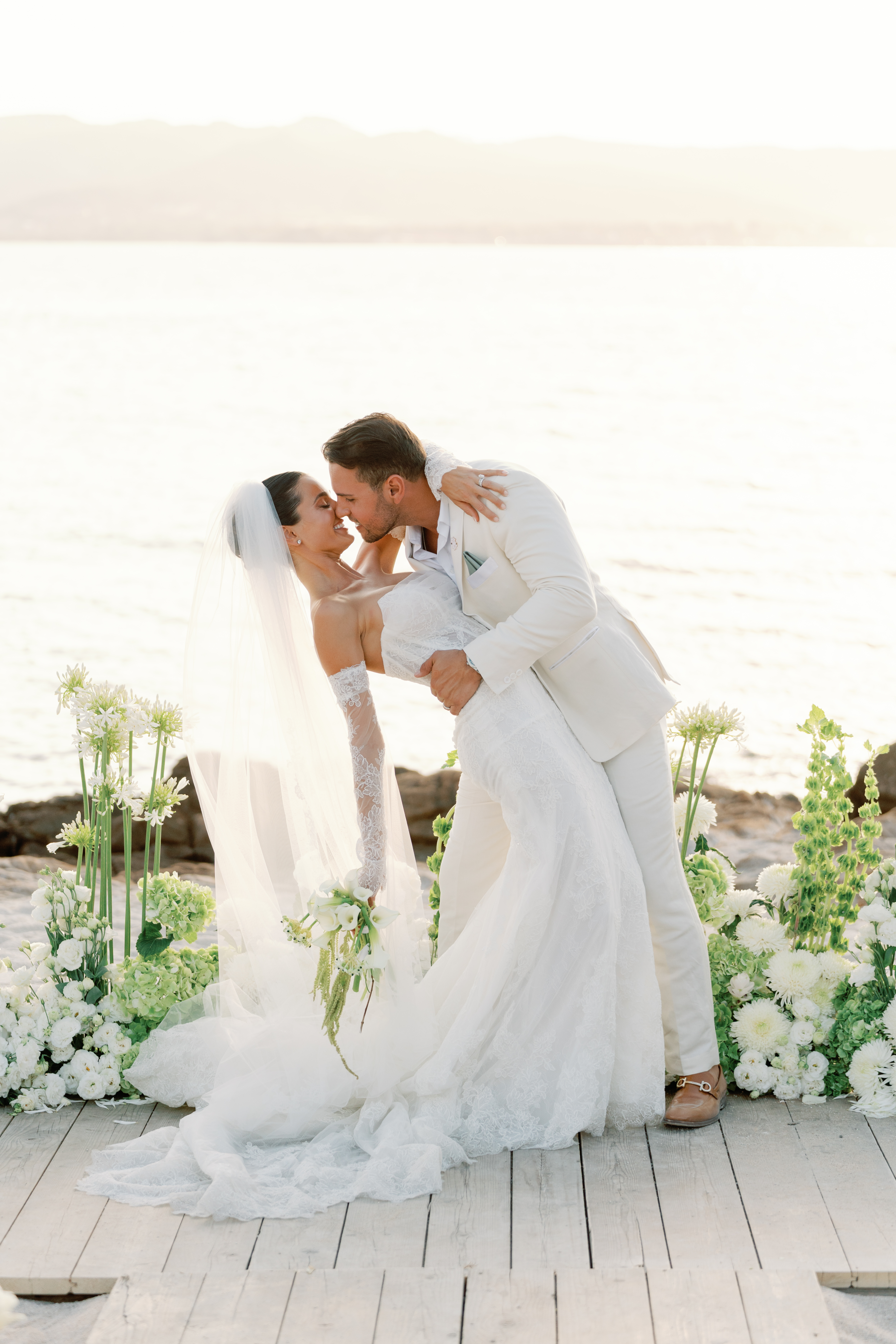 Bride and groom kissing during a seaside wedding ceremony at 7Pines Resort Sardinia, with floral arrangements and bright Mediterranean light.